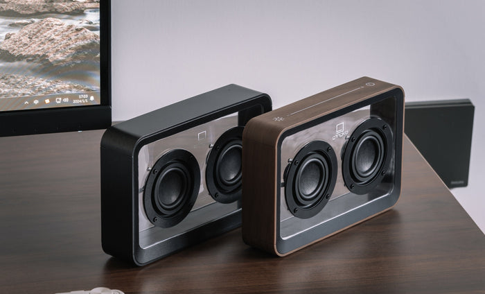 Pair of walnut see-through speakers with two black drivers each on desk