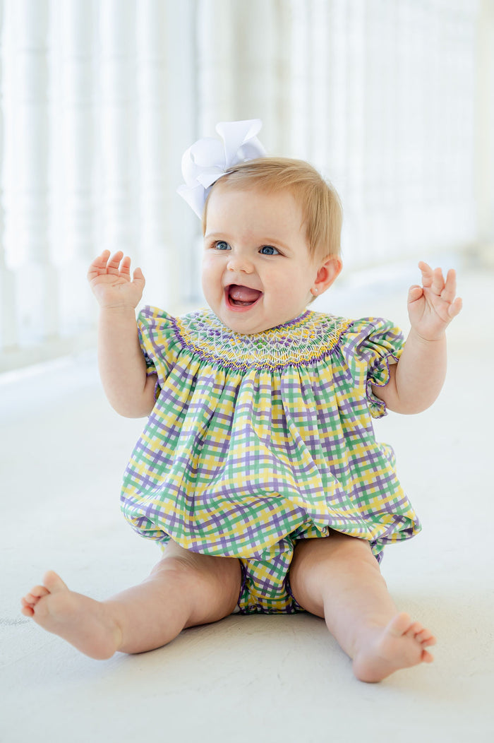 A baby girl wearing the smocked bubble embodies the joyful spirit of Mardi Gras with its bold colors and playful details.