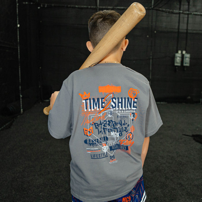Child wearing a gray t-shirt with colorful text and graphics, holding a baseball bat.