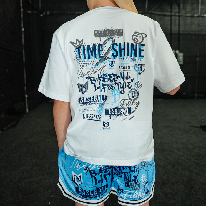 Person wearing a white t-shirt with blue graphics and text, standing in an indoor setting.