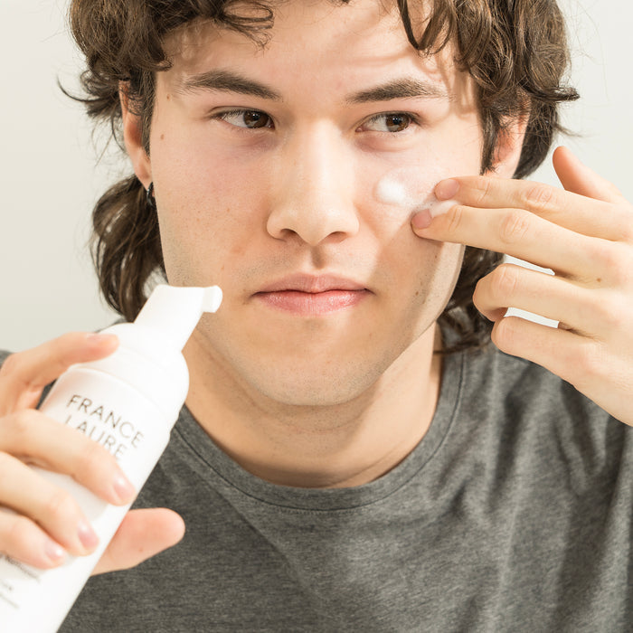 Man applying France Laure skincare cream to cheek, showcasing daily face care routine for all skin types