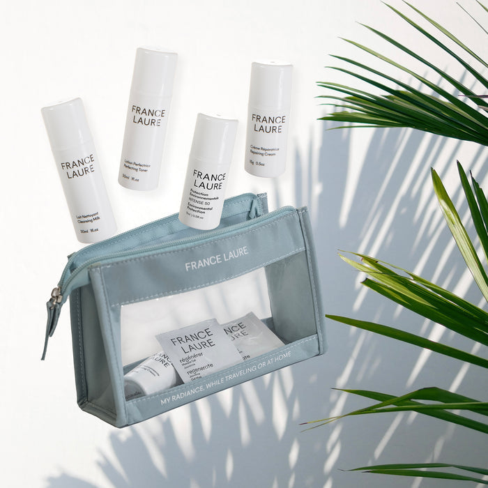 France Laure travel skincare set with cleansing milk, toner, repair cream, and gel mask in a clear pouch, styled with palm leaves for radiant skin care.
