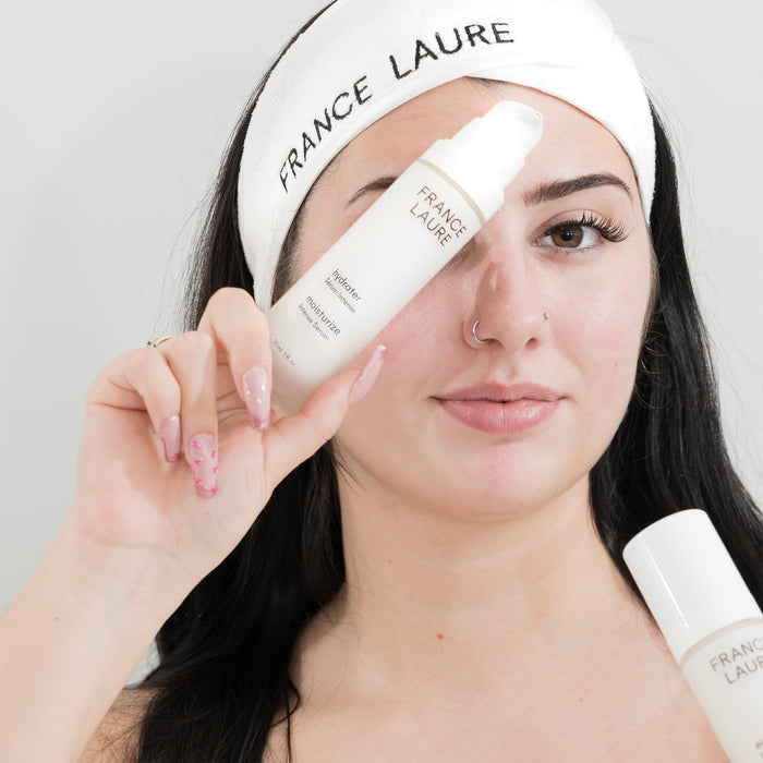 Woman holding France Laure hydrater moisturize intense serum, showcasing skincare product with clean, radiant skin and branded headband.