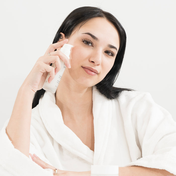 Woman in white robe applying hydrating facial serum for glowing skin, gentle skincare routine for all skin types