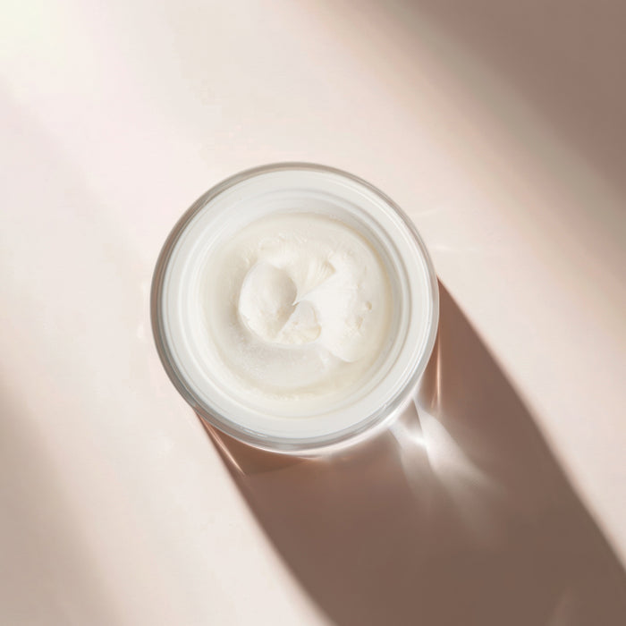 Luxurious white face cream in clear jar with smooth texture, ideal for all skin types and ages, shown under soft natural light.