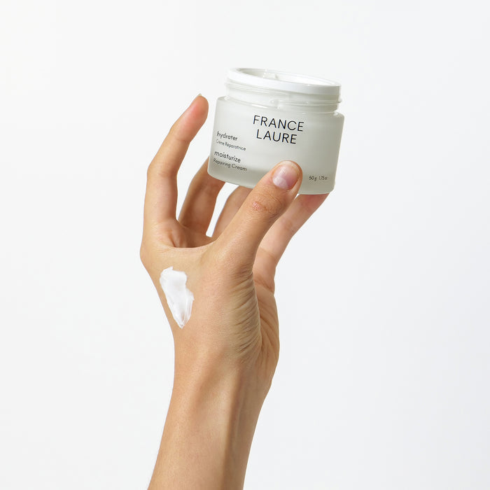 Hand holding France Laure Moisturize Repairing Cream jar with swatch on skin, showcasing rich texture for dry skin hydration