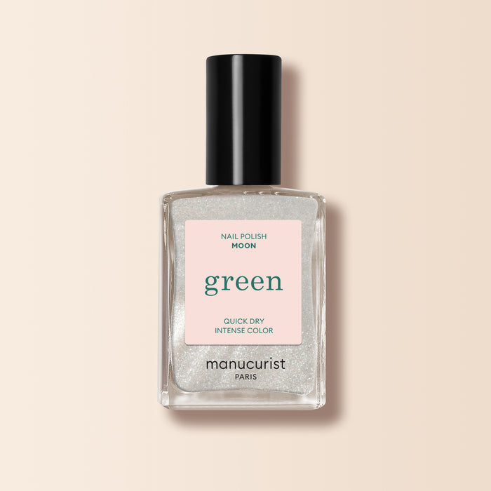 A bottle of Manucurist Moon nail polish features a pearly white, clear liquid with shimmer, black cap, and light pink label from the Green™ range, displayed on a beige background.