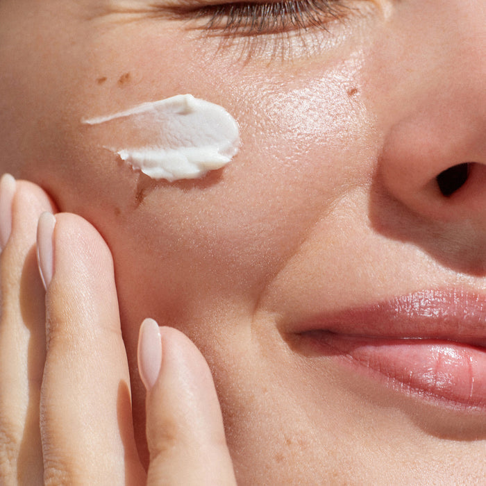 Close-up of woman applying rich white face cream to cheek, showcasing smooth texture and radiant skin for daily skincare routine