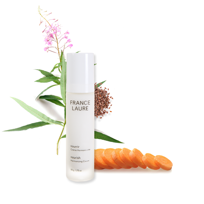 France Laure Nourish Harmonizing Cream bottle with carrot slices, flax seeds, and pink flowers, showcasing natural skincare ingredients for all skin types.