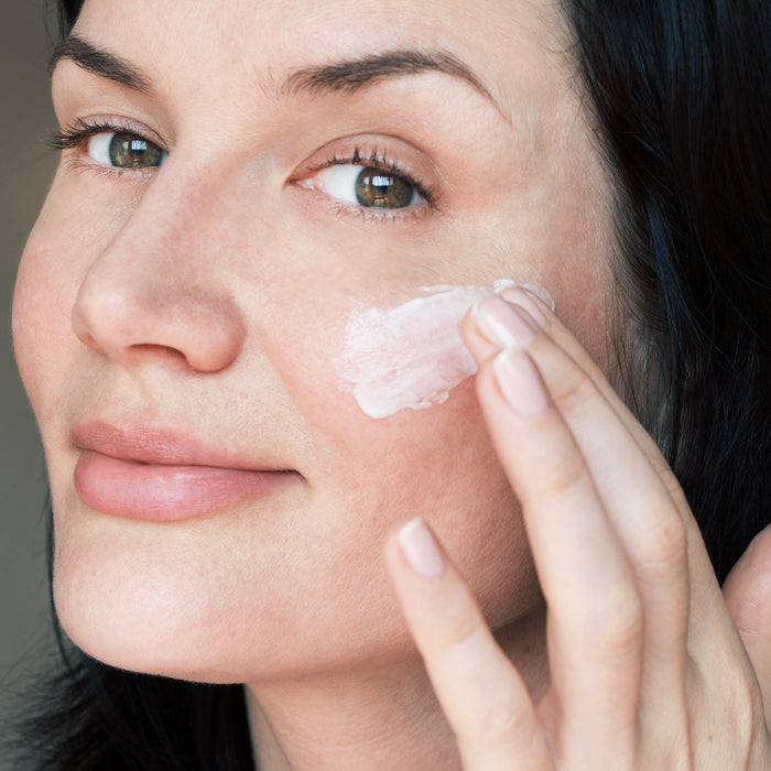 Woman applying gentle facial cream to cheek, showcasing smooth skincare routine for all skin types and ages