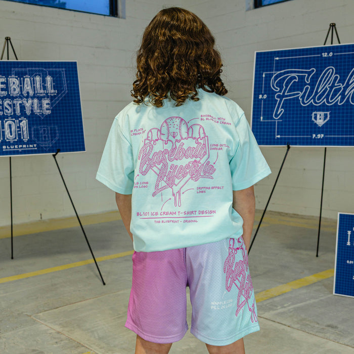 Person wearing a light blue t-shirt with pink ice cream graphic and "Baseball Lifestyle 101" logo, standing in front of blueprints.