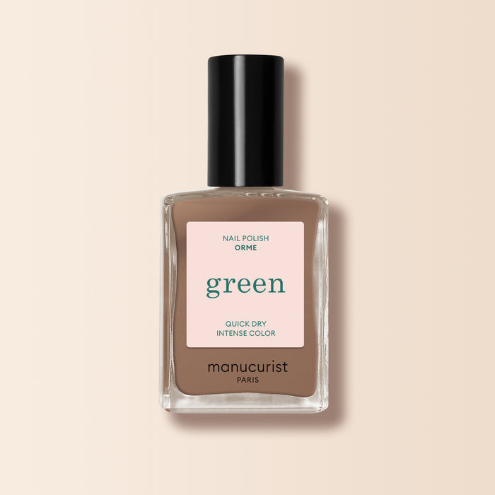 A bottle of Manucurist Orme nail polish from the Green™ range, in a café au lait light brown shade with quick-dry, intense color, black cap, and minimalist label displayed on a beige background.