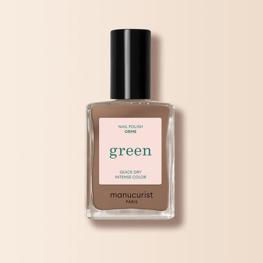 A bottle of Manucurist Orme nail polish from the Green™ range, in a café au lait light brown shade with quick-dry, intense color, black cap, and minimalist label displayed on a beige background.