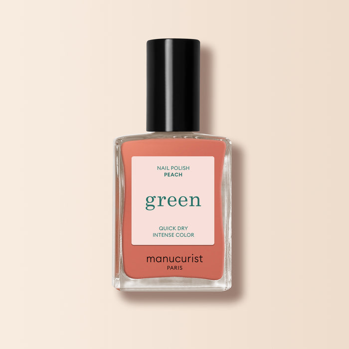 A bottle of Manucurist nail polish in the shade Peach, with a black cap and peach label featuring white and green text, set on a light beige background. Ideal for adding a subtle summer tint to your nails.