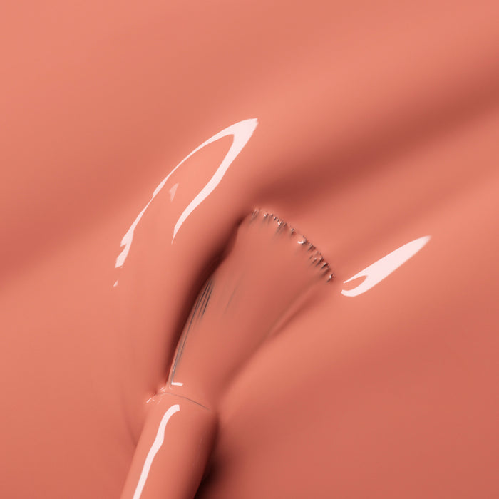 A close-up of a brush gliding through Manucurist's Peach, showing its glossy summer peach tint, smooth texture, and highlights reflecting off the surface.