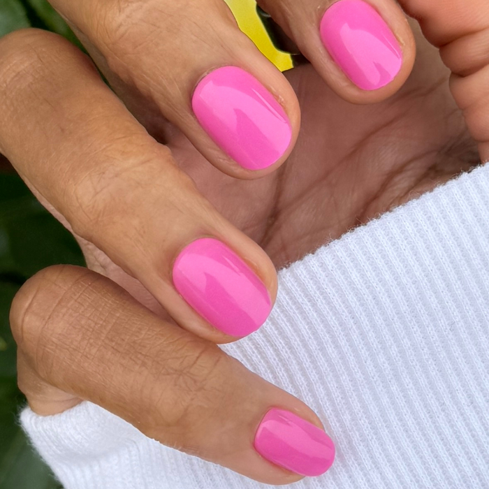 Peony | Extra Short | Round - Tab Press-On nails in bright pink glossy finish shown on hand with white sleeve background