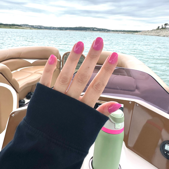 Peony | Extra Short | Round - Tab Press-On nails in bright pink glossy finish shown on hand outdoors by the water