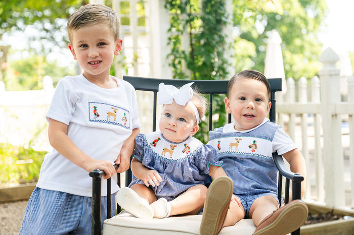 Baby girl wearing Smocked Hunting Season Bubble by Ruth and Ralph sitting with sibling in matching smocked outfit outdoors