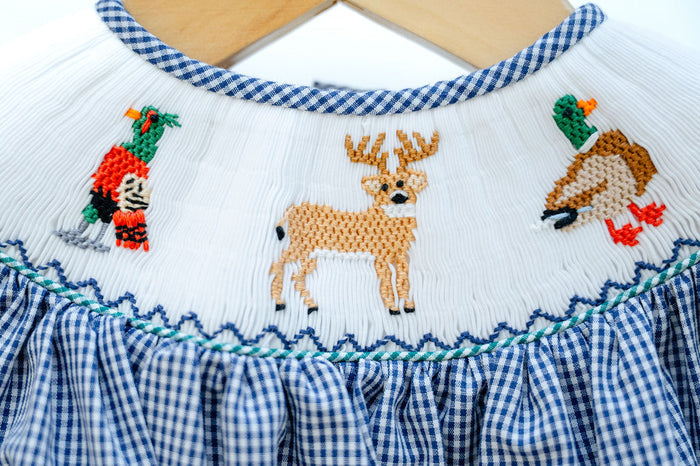 Close-up of smocked hunting embroidery detail on Ruth and Ralph blue gingham dress, featuring deer and pheasant