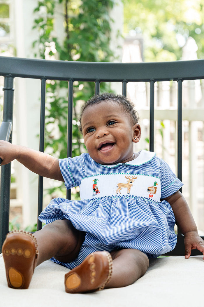 Close-up of baby smiling in Smocked Hunting Bubble by Ruth and Ralph, showing smocked deer and duck detail