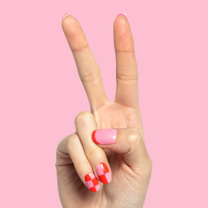 Pink Checker Party | Short | Round - Tab Press-On showing hand with pink and red checker mani against solid pink background