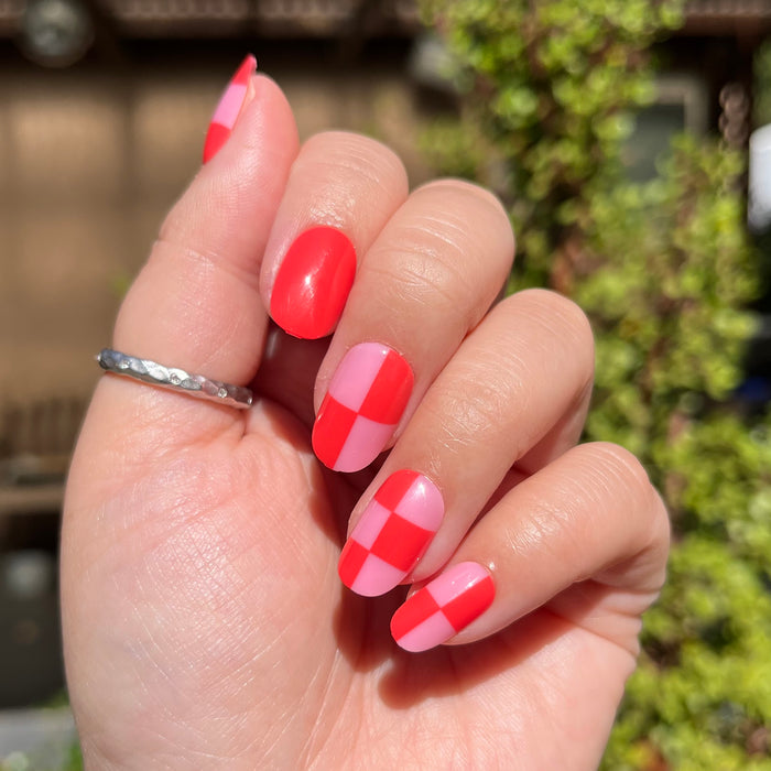 Pink Checker Party | Short | Round - Tab Press-On showing hand with pink and red checker false nails in natural sunlight outdoors