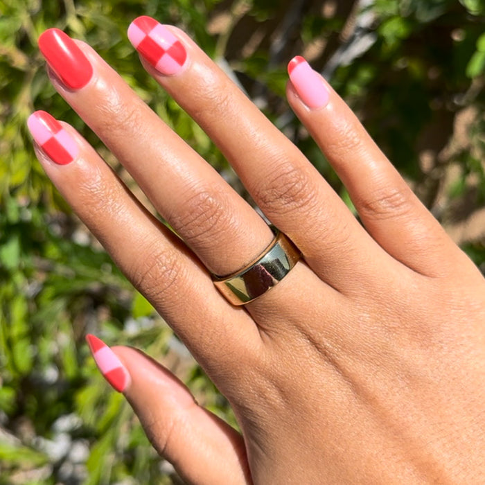 Pink Checker Party | Short | Round - Tab Press-On showing hand with pink and red checker mani outdoors in natural sunlight