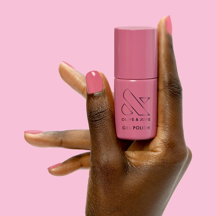 Prom - Gel bottle held between fingers with matching soft pink gel polish for an elegant at-home manicure by Olive and June