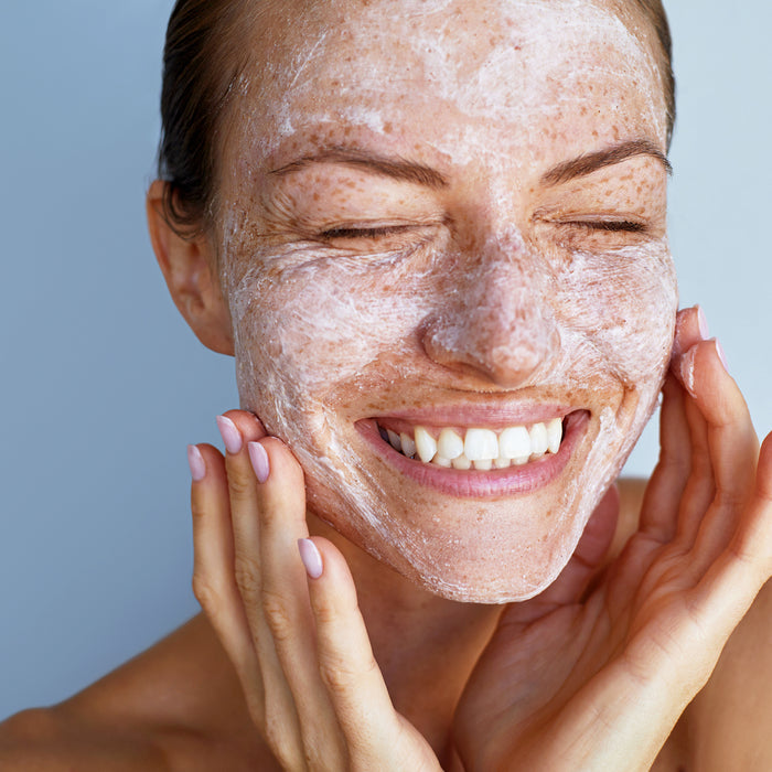 Woman smiling with gentle exfoliating face scrub applied, showcasing radiant skin texture and natural freckles for skincare routine