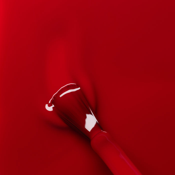 A close-up of the Manucurist Red Cherry nail polish brush, coated in glossy red polish, set against a vibrant red background.