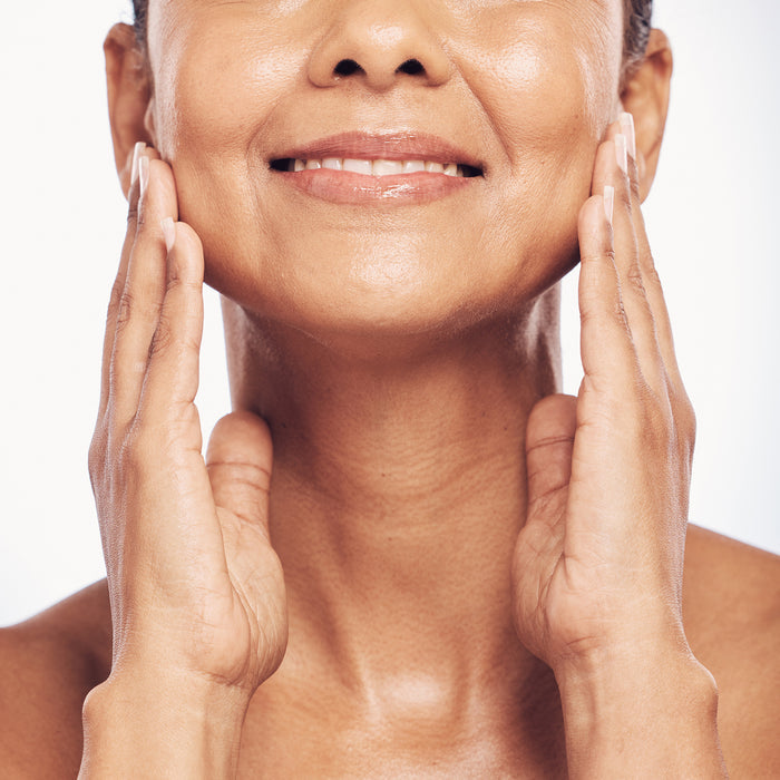Woman gently touching radiant, smooth skin on her face and neck, showcasing natural glow and healthy complexion for all skin types.
