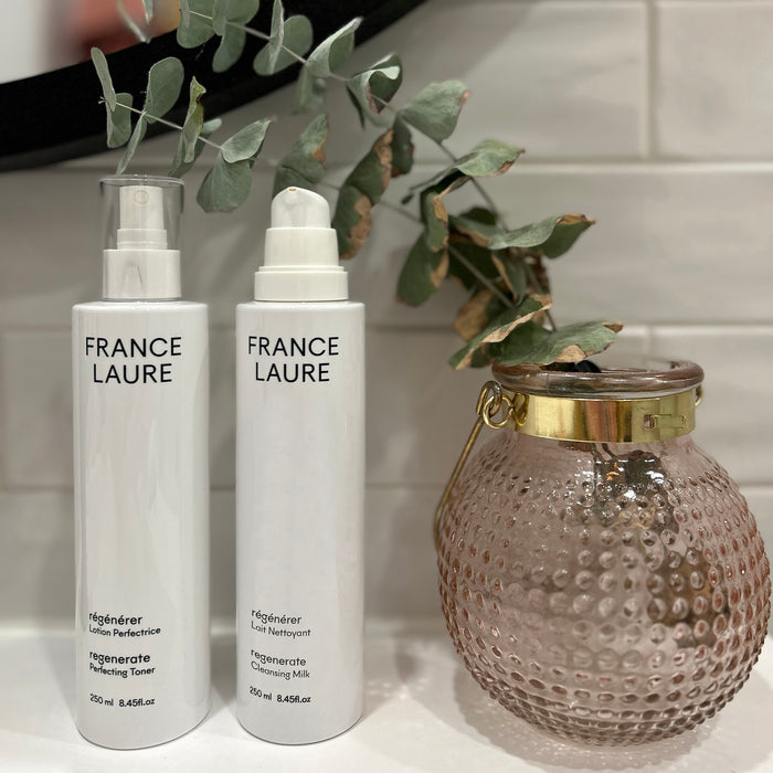 France Laure Regenerate Perfecting Toner and Cleansing Milk bottles beside textured vase with eucalyptus, white tile background