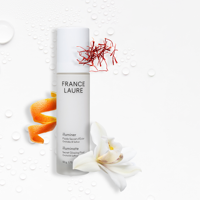 France Laure Illuminate Secret Glowing Fluid with orchid & saffron, shown with orange peel, white orchid, and water droplets on white background