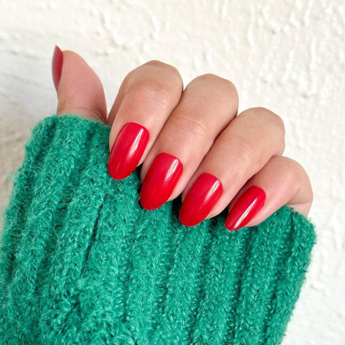 Hand wearing green sleeve with medium oval nails in blue-toned red shade Secret Recipe - Press-On | Medium | Oval