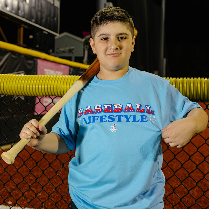 Light blue baseball youth tee, 4th of July outfit with red and blue Baseball Lifestyle graphic.
