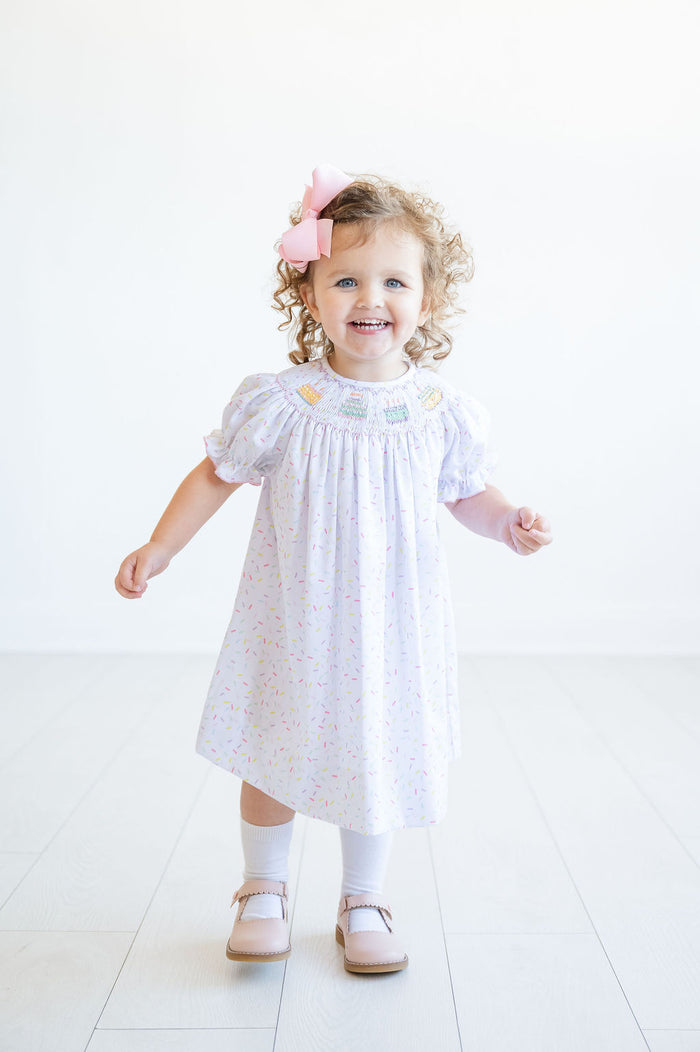 With its sprinkle pattern and delicate smocked cake design, this dress is a standout piece for your birthday girl.