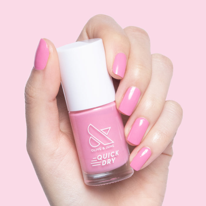 Hand holding Olive and June Taffy quick dry nail polish bottle with bright pink nails against pale pink background
