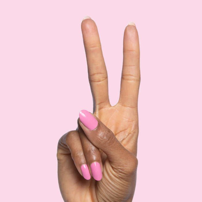 Hand showing peace sign with nails painted in bright pink Taffy quick dry gel polish on pale pink background