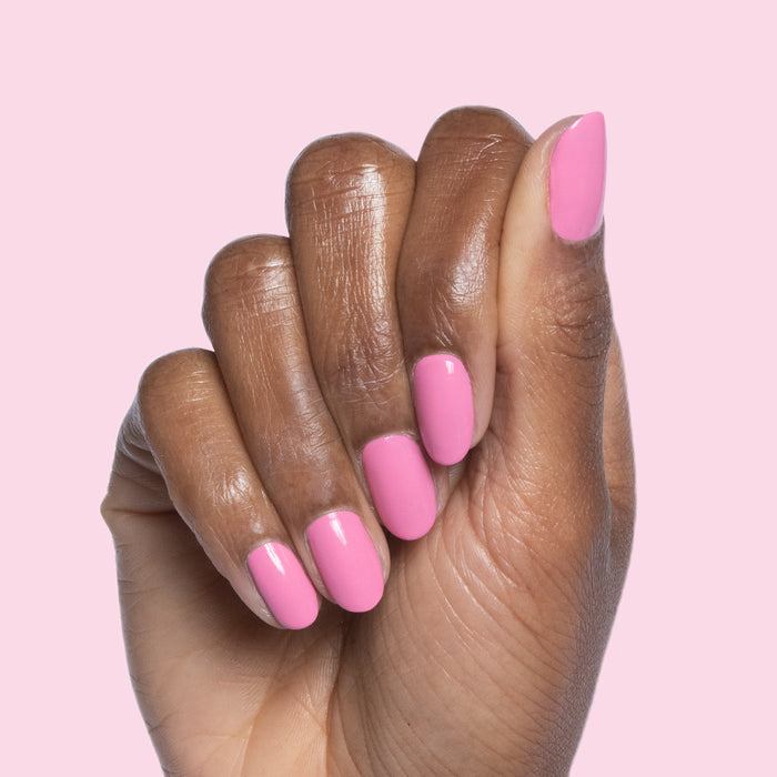Hand with nails painted in bright pink Taffy quick dry gel polish against soft pink background