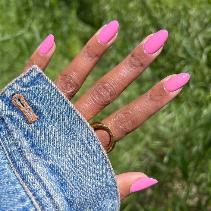 Hand outdoors with nails painted in bright pink Taffy quick dry gel polish wearing a gold ring and denim jacket sleeve