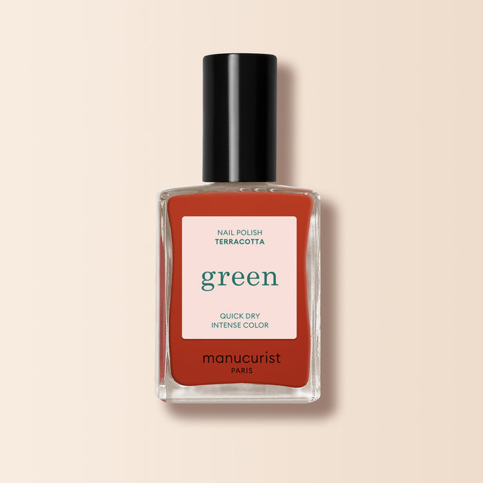 A bottle of Manucurist Terracotta nail polish in a scorched red earth shade, featuring a black cap and quick dry intense color label, displayed against a light beige background.