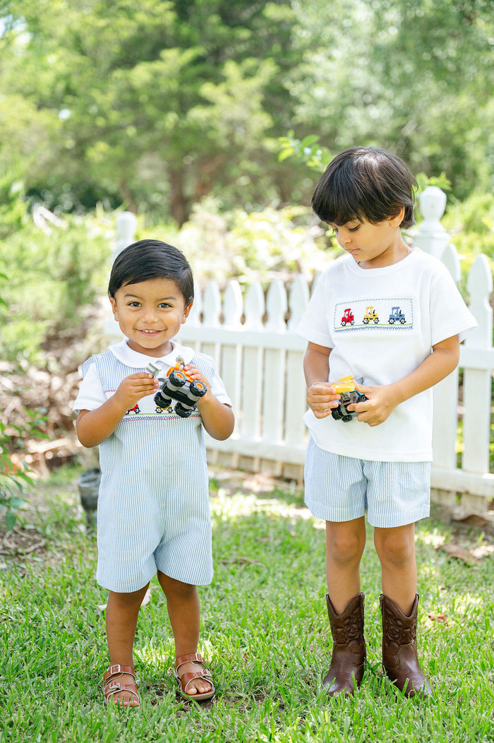 Two boys wearing Ruth and Ralph outfits outdoors, one in Smocked Tractor Jon Jon, one in matching smocked t-shirt