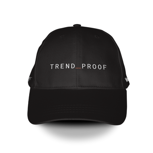 Black baseball cap with “TREND_PROOF” embroidered in white across the front, featuring a red underscore between the words.