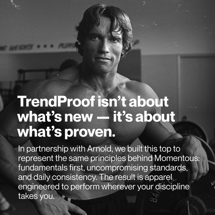 Black-and-white archival-style photograph of Arnold Schwarzenegger in a gym setting, shown from the waist up with muscular build, slightly sweaty hair, and intense expression. He stands shirtless holding a weight plate, conveying strength and discipline. Overlaid white text reads: “TrendProof isn’t about what’s new — it’s about what’s proven.” Below, smaller text explains the collaboration with Arnold and Momentous, emphasizing fundamentals, uncompromising standards, and daily consistency.