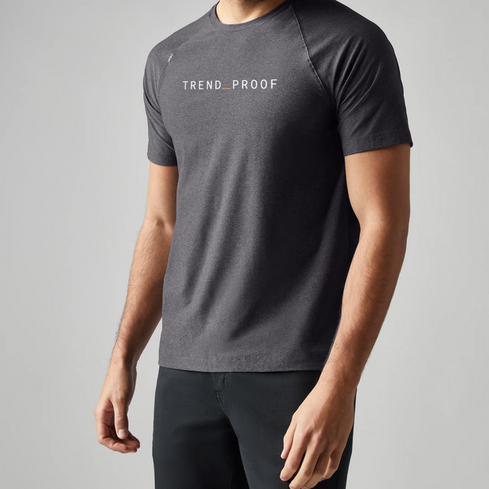 Front view of a man wearing a gray short-sleeve athletic t-shirt with “TREND_PROOF” printed across the chest in white lettering with a red underscore.