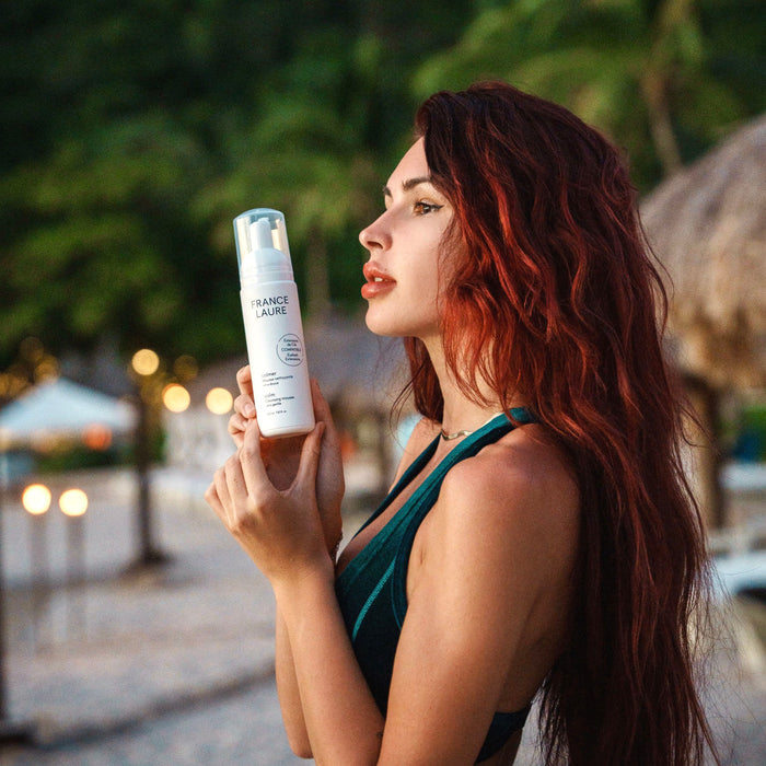 Woman holding France Laure Calm Cleansing Mousse, gentle facial cleanser for sensitive skin, outdoor tropical setting